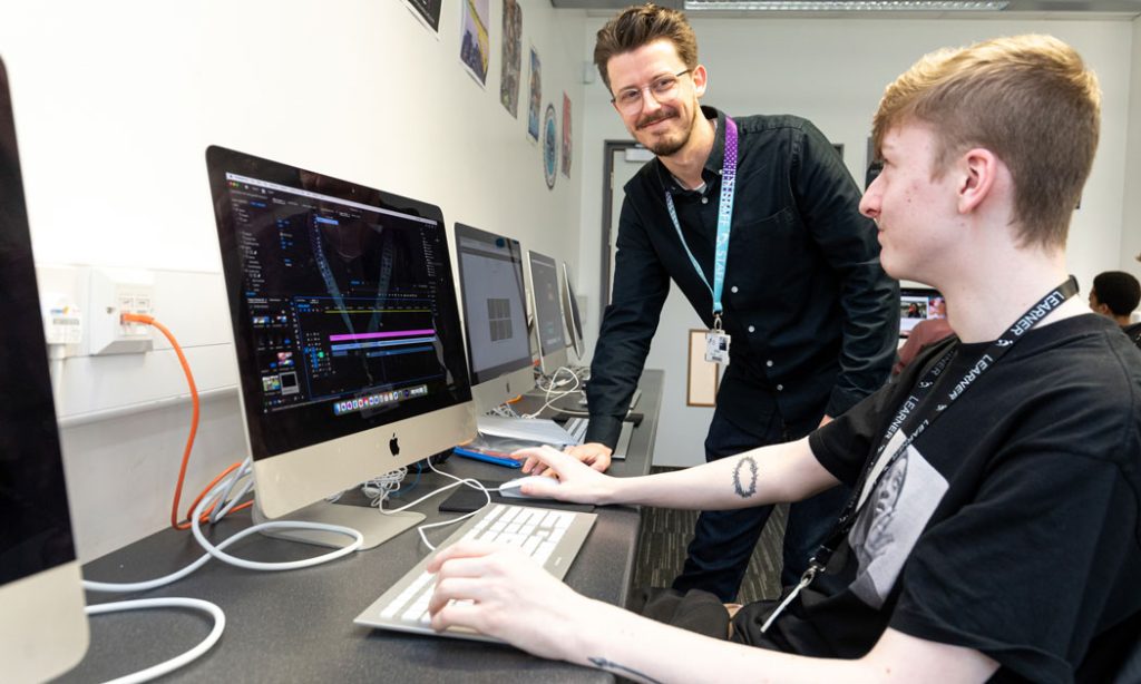 Learner at computer with tutor looking on.