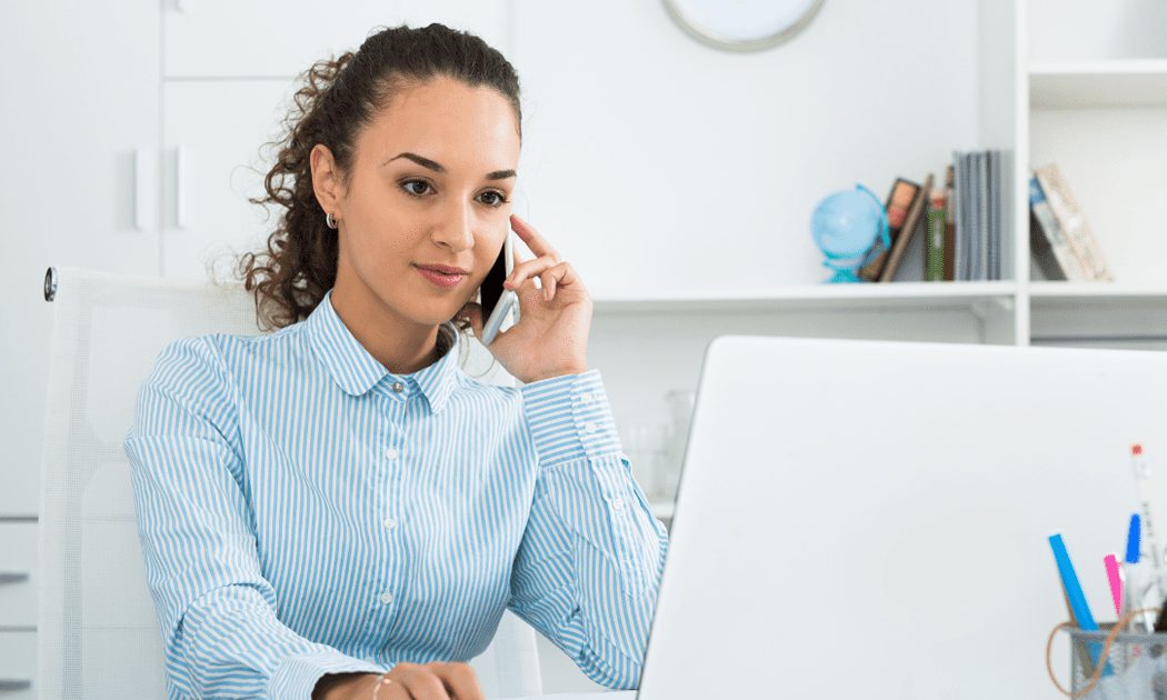 Lady on a mobile phone sat looking at a computer screen